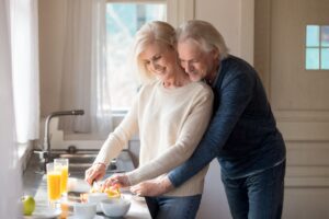 elderly couple embracing a hug while woman is cutting an orange