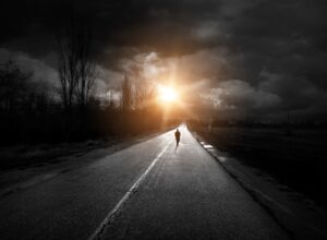 man walking on dark street with bright light at the end