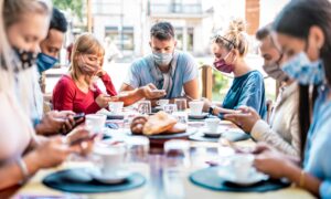 people sitting at a table having dinner while wearing masks and looking at their phones